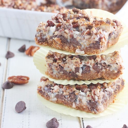 Three cut Hello Dolly bars stacked on top of each other on a white wooden table