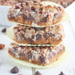 Three cut Hello Dolly bars stacked on top of each other on a white wooden table