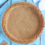 baked graham cracker pie crust against a blue wooden background with a pie serve and graham crackers to the side