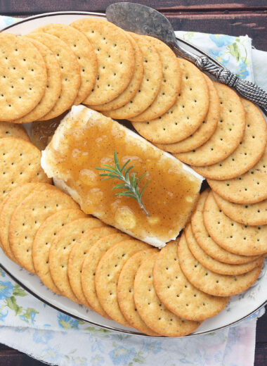 overhead view of block of cream cheese on a floral China plate covered in Jezebel sauce surrounded by crackers