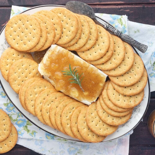 overhead view of block of cream cheese on a floral China plate covered in Jezebel sauce surrounded by crackers