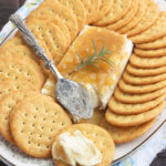 block of cream cheese on a floral China plate covered in Jezebel sauce surrounded by crackers