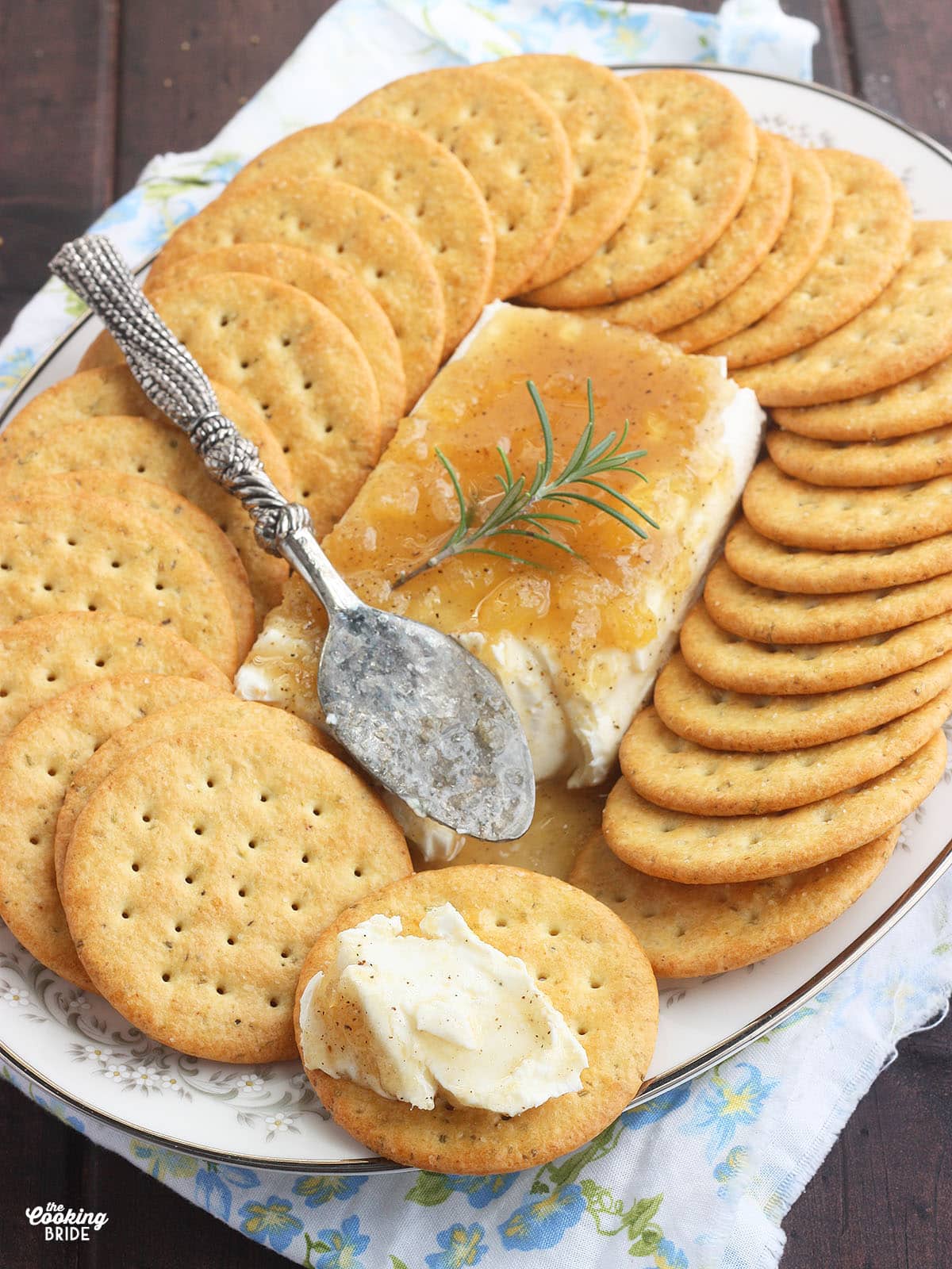 block of cream cheese on a floral China plate covered in Jezebel sauce surrounded by crackers