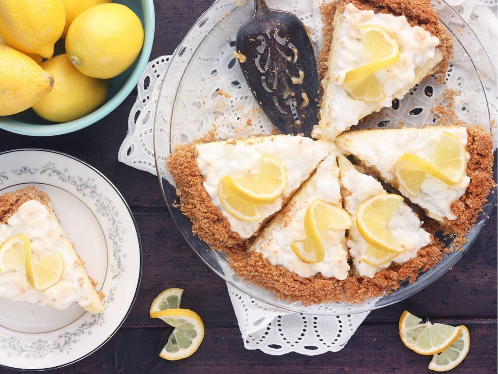 sliced lemon icebox pie with a plated piece of pie and a bowl of lemons to the side
