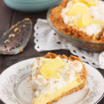 a slice of lemon icebox pie on a floral plate with the pie and a bowl of lemons in the background