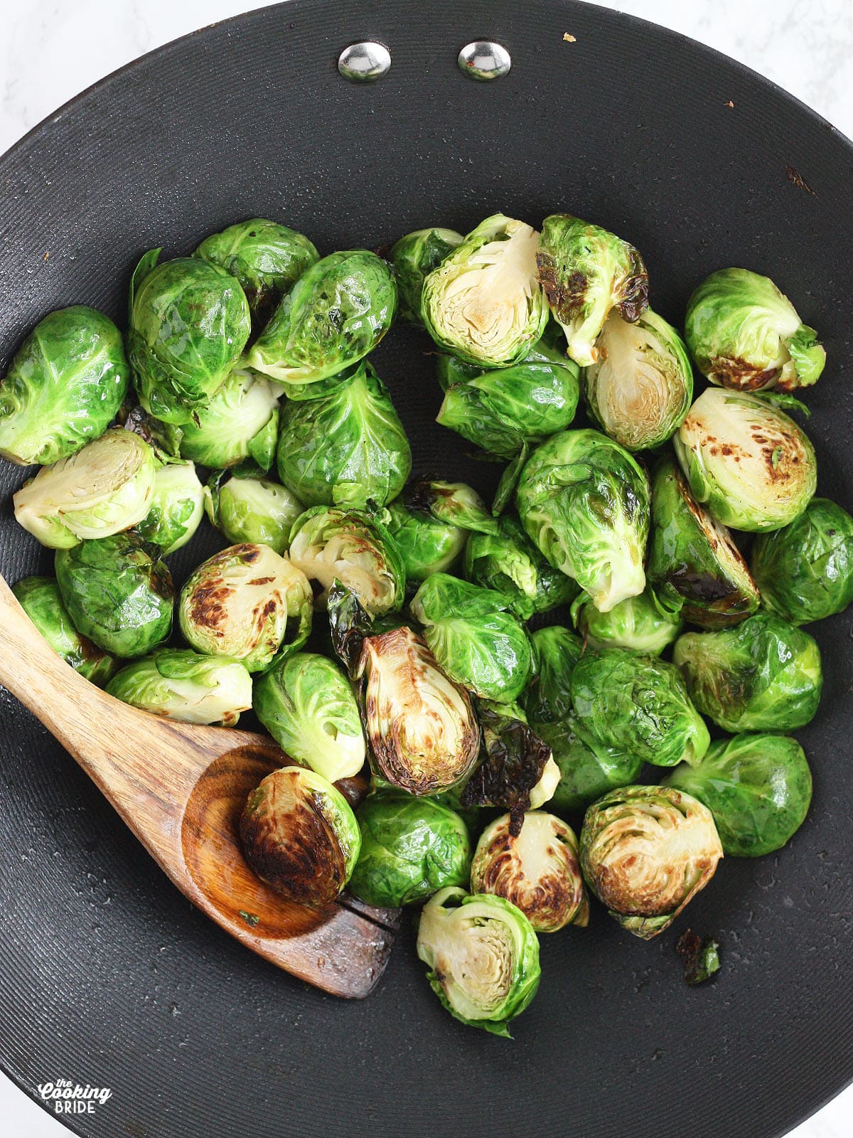 lightly charred Brussels sprouts cooking in a wok with a wooden spoon