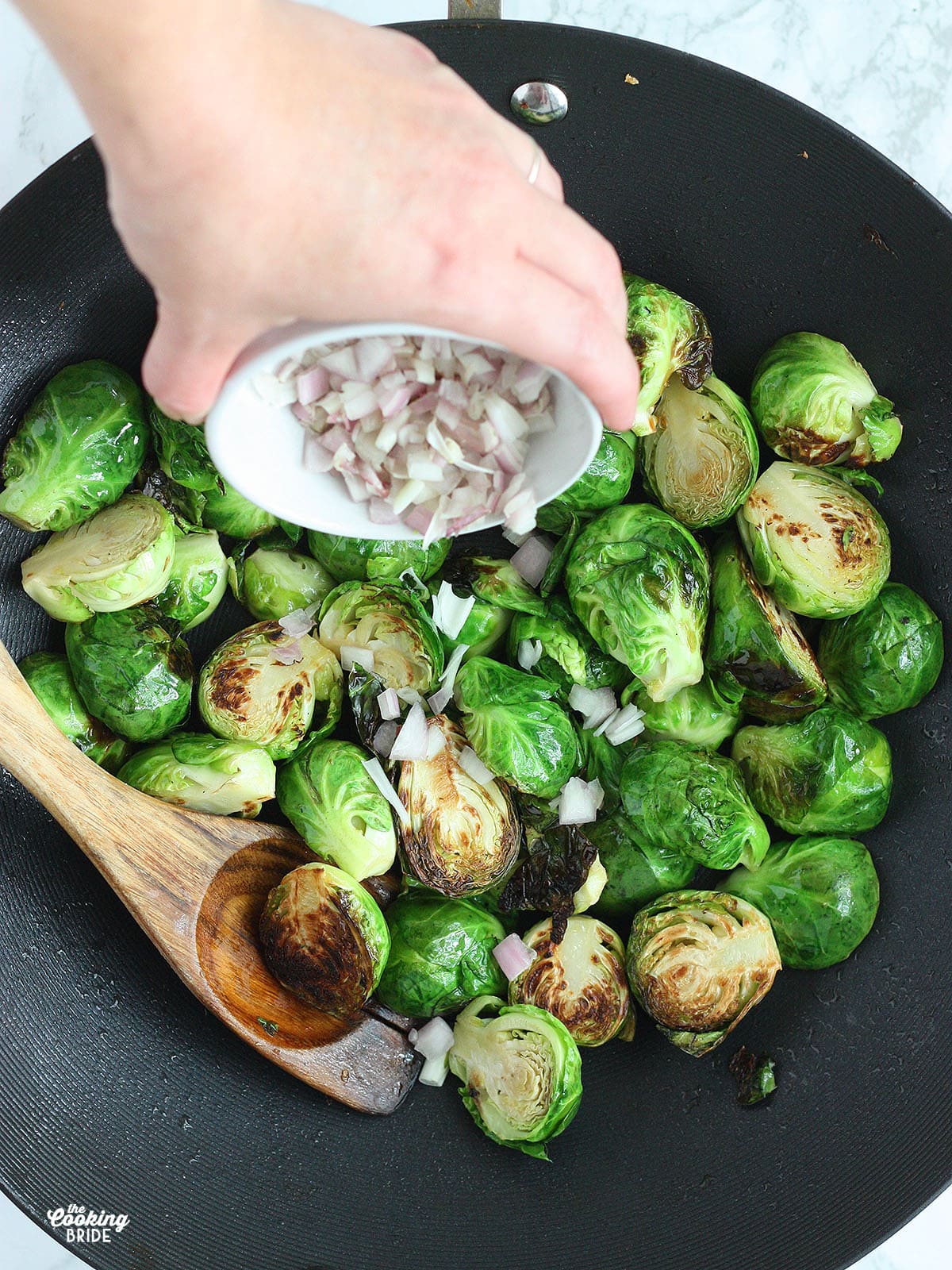 hand adding shallots to Brussels sprouts frying in a wok