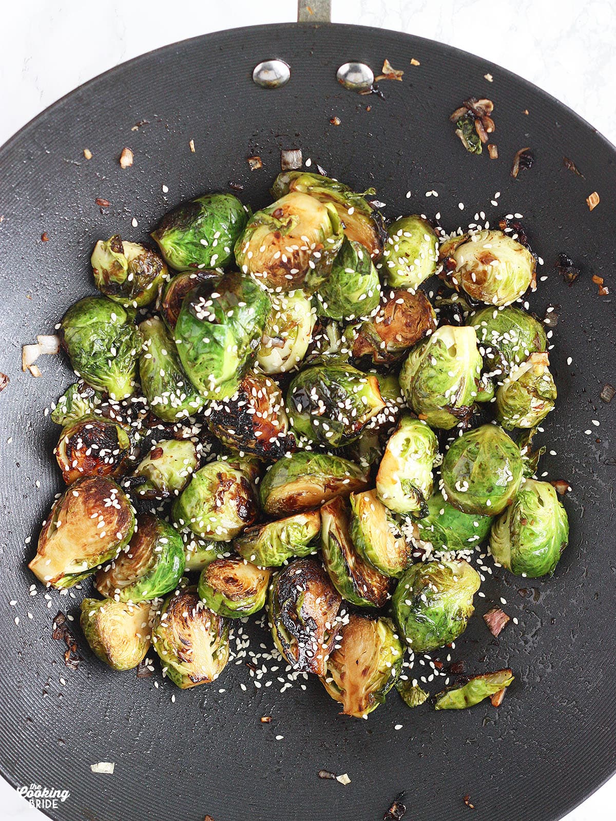Stir Fried Brussels sprouts garnished with sesame seeds in a wok.