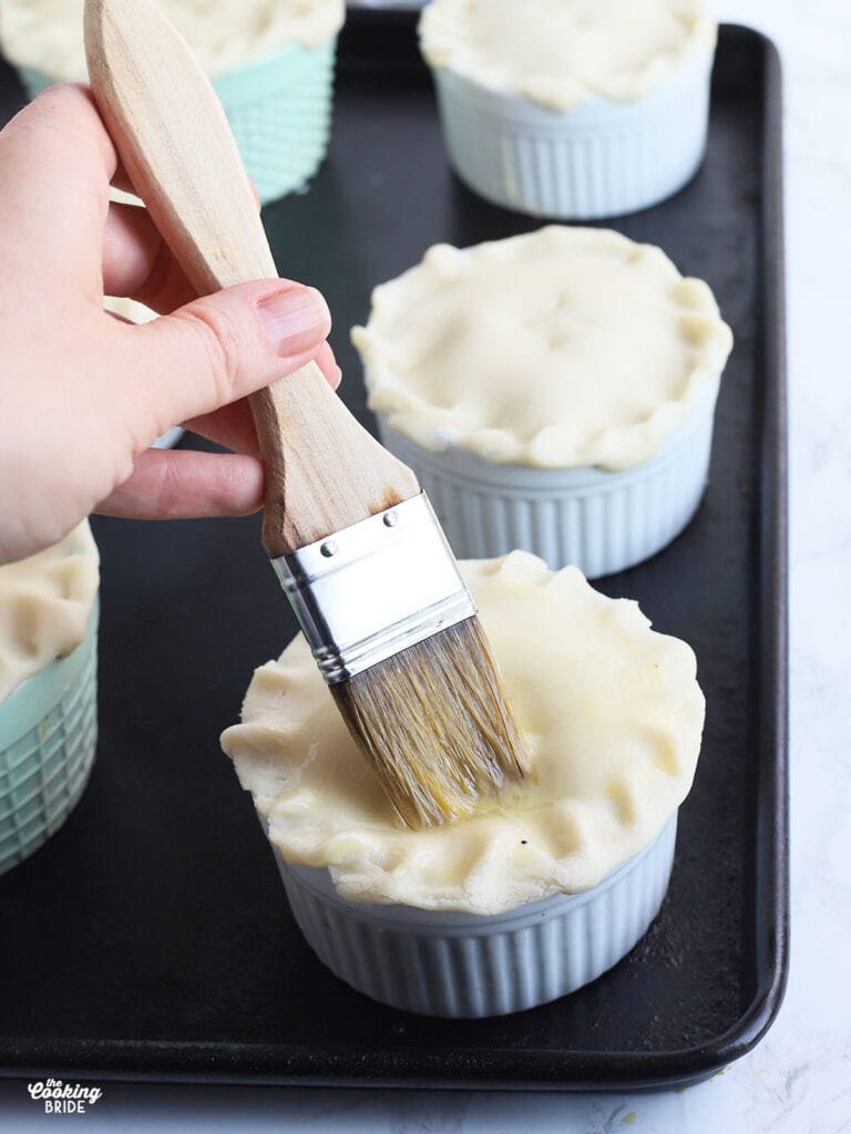 hand using a pastry brush to apply egg wash to the crust of a mini pot pie