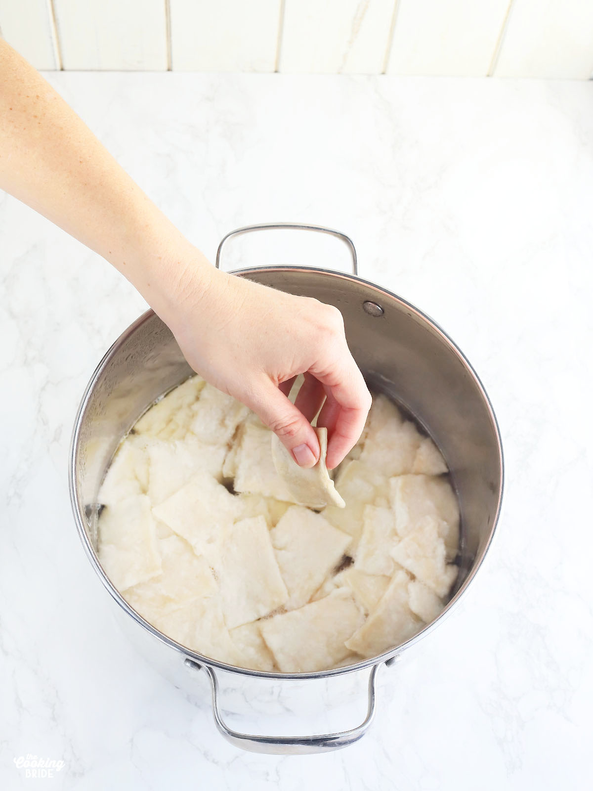 hand dropping a dumpling into a stock pot full of dumplings
