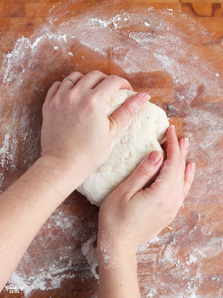 pair of hands kneading dumpling dough on a wooden cutting board