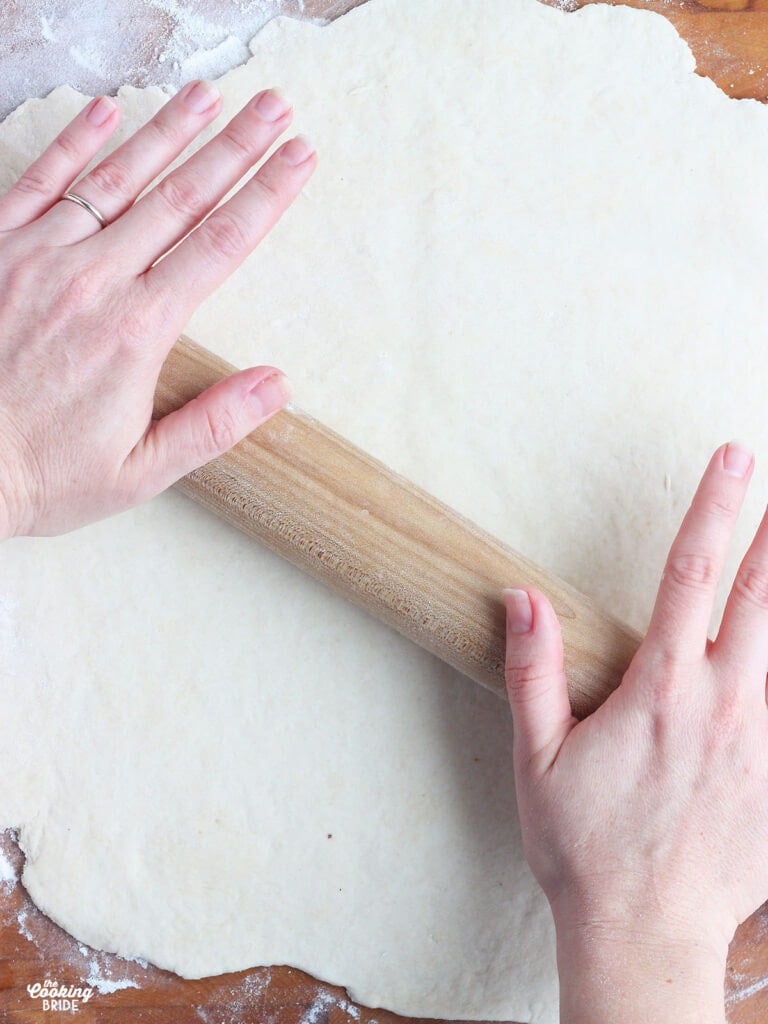 pair of hands rolling out dumpling dough on a wooden cutting board