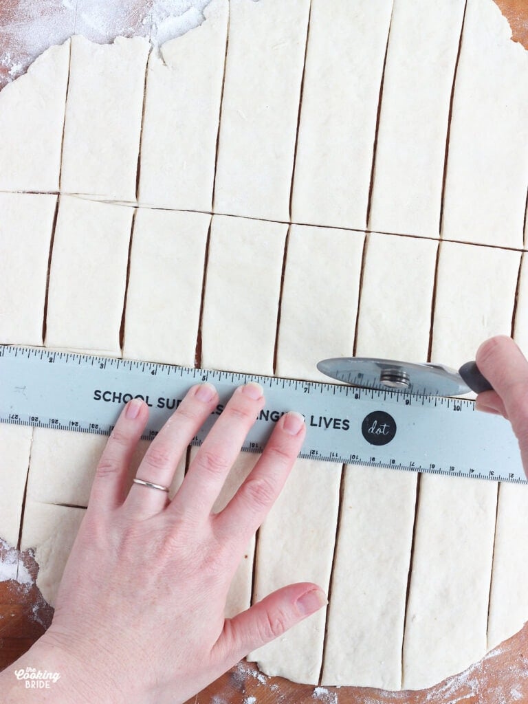 pair of hands using a pizza cutter and a ruler to cut dumplings