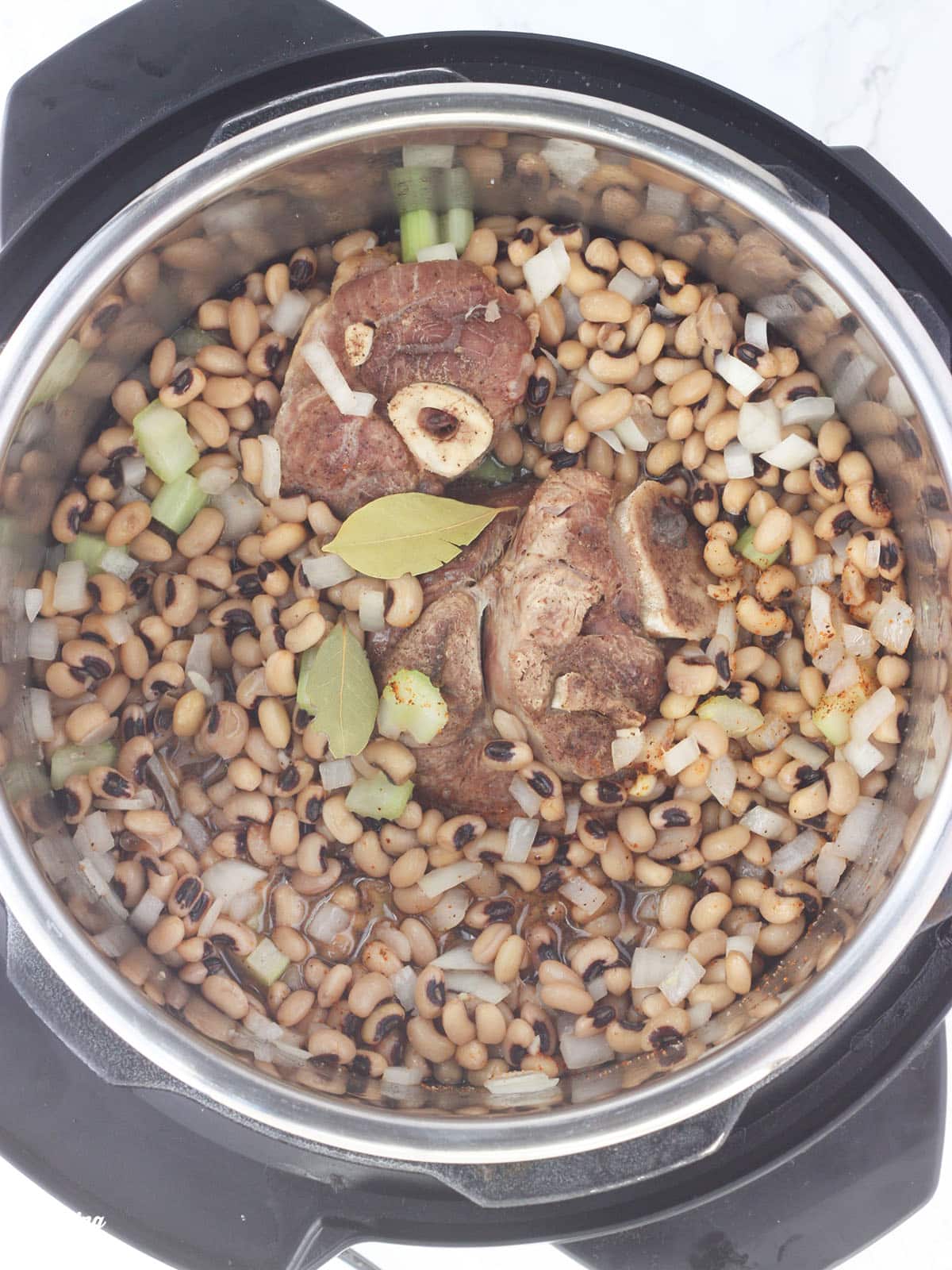 overhead shot of black-eyed peas, ham hock and bay leaves in an Instant Pot