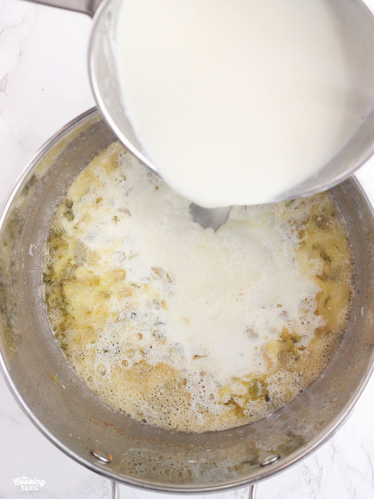 milk and heavy cream being poured from a saucepan into a stockpot of sautéed vegetables