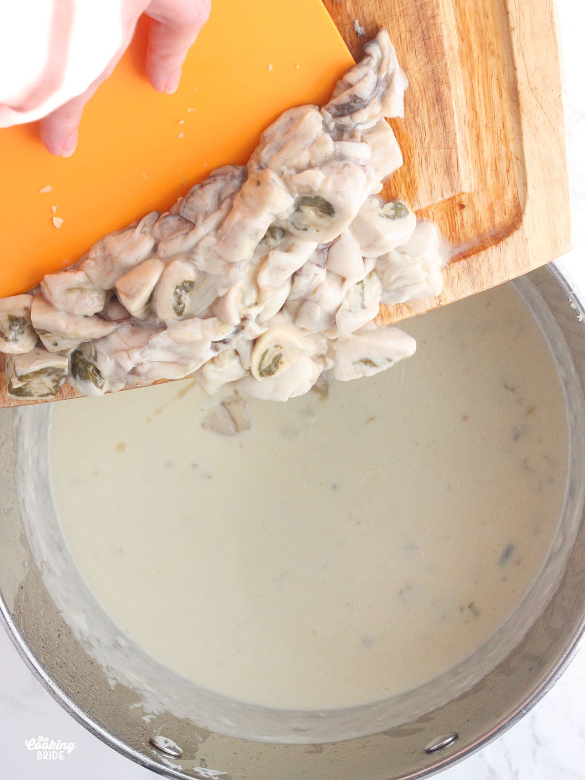 hand pushing raw oysters off of a cutting board and into a pot of heavy cream and milk