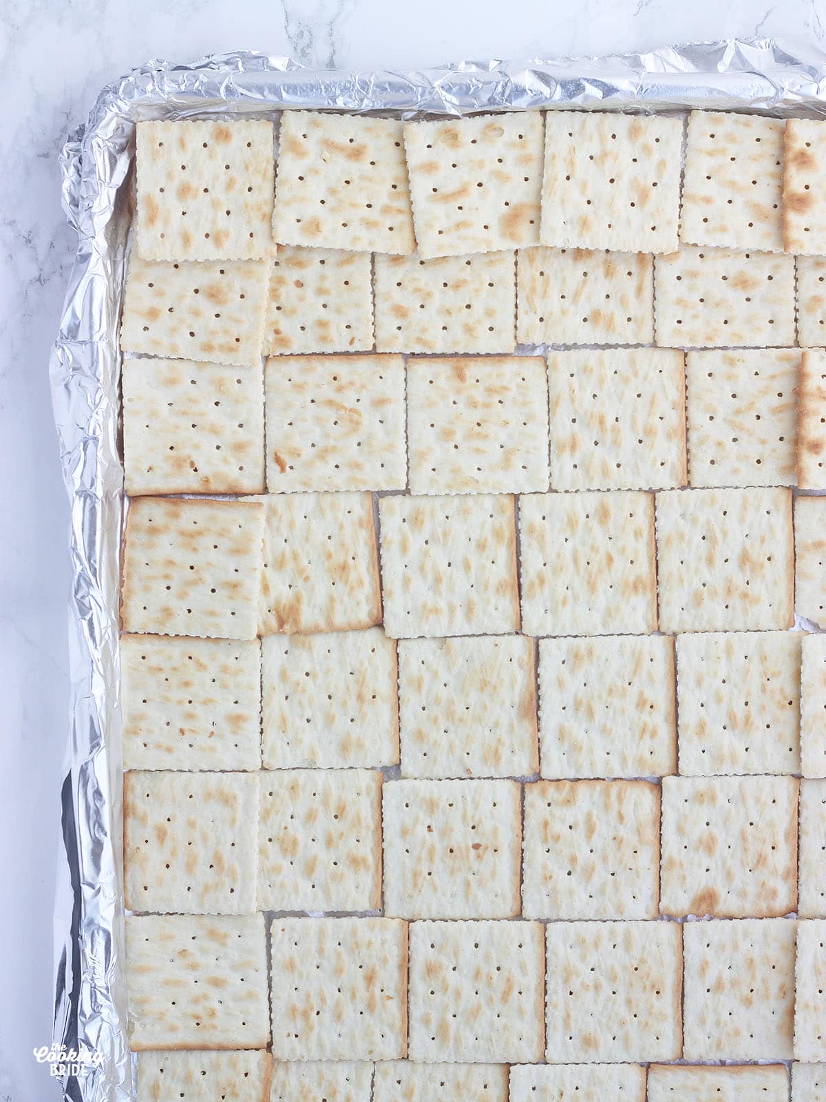 saltine crackers lined up in a single layer on a foil lined baking sheet