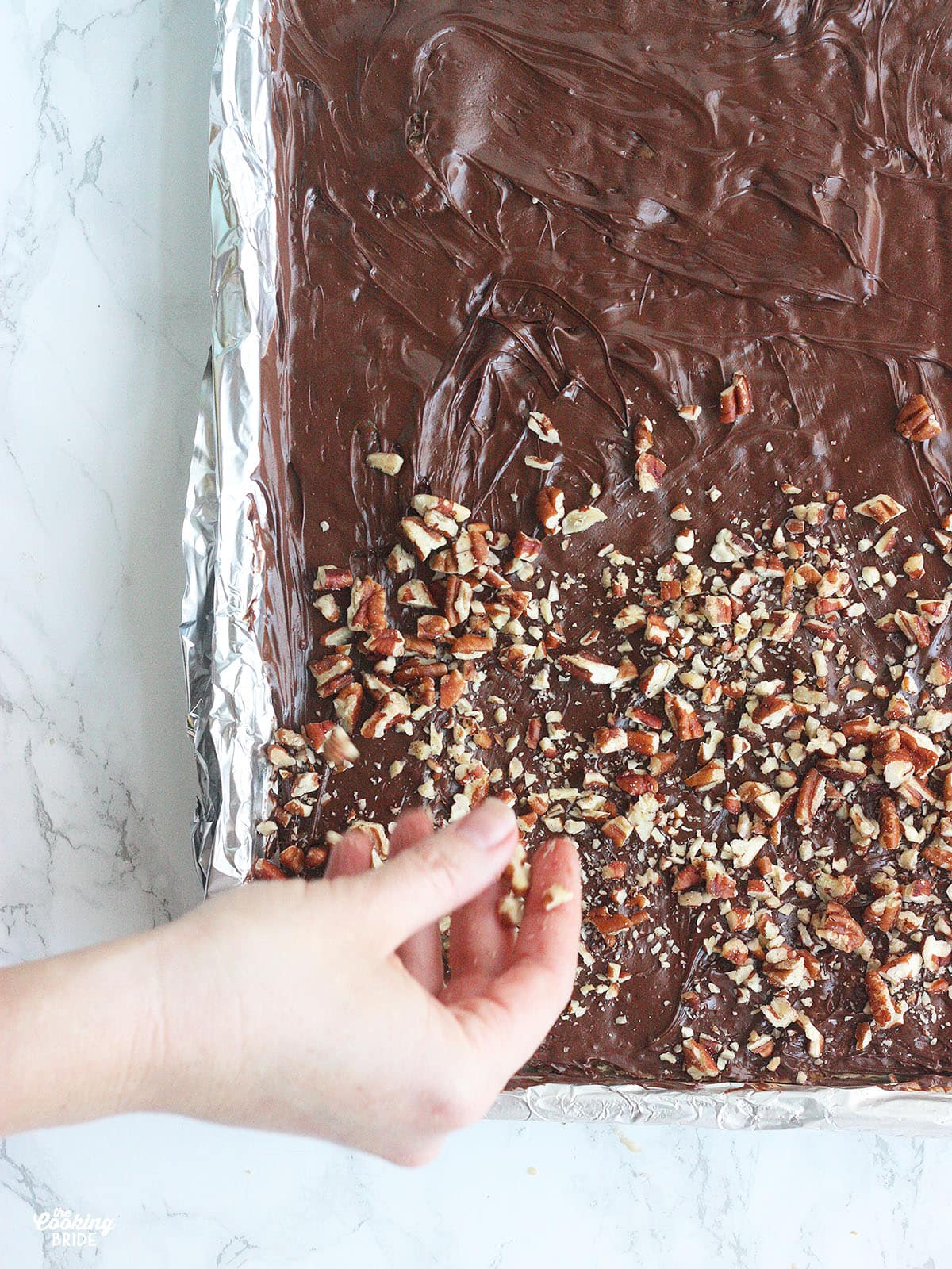 hand spreading chopped pecans over melted chocolate
