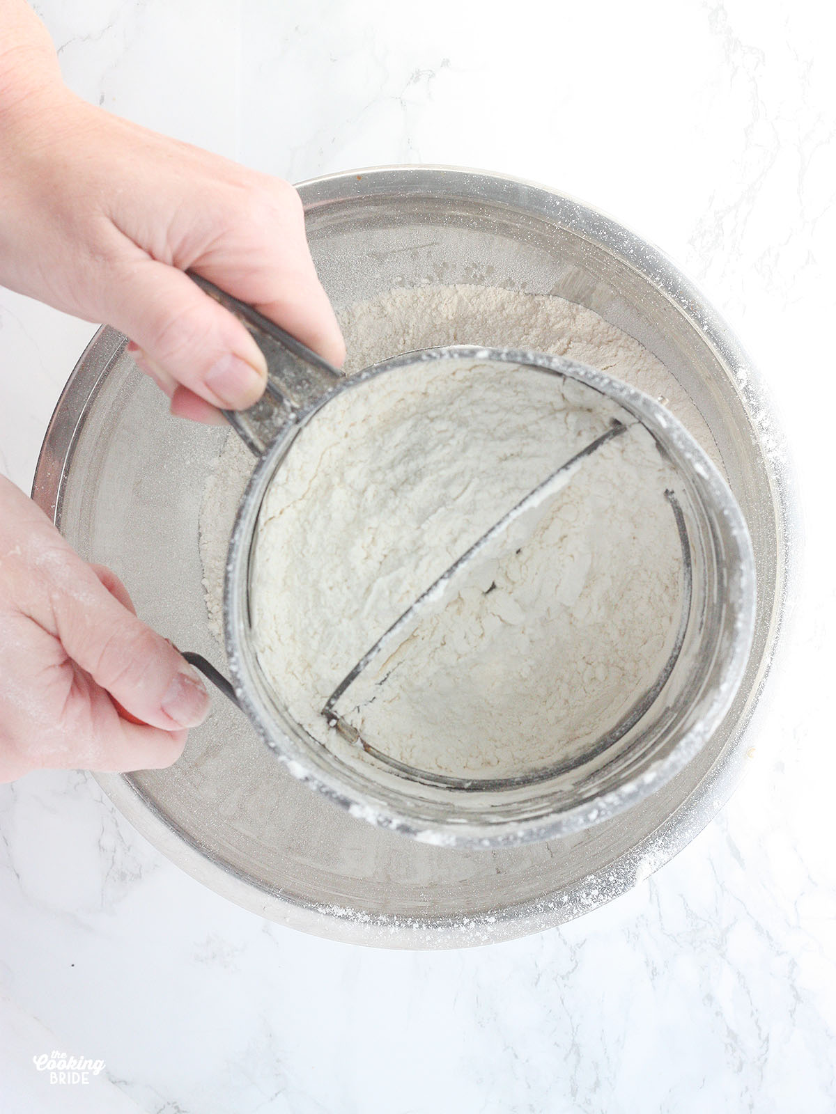 hands sifting flour, baking soda and salt into a metal mixing bowl
