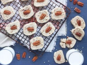 baked butter pecan cookies on a baking rack with two glasses of milk to the side