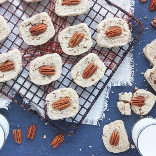 baked butter pecan cookies on a baking rack with two glasses of milk to the side