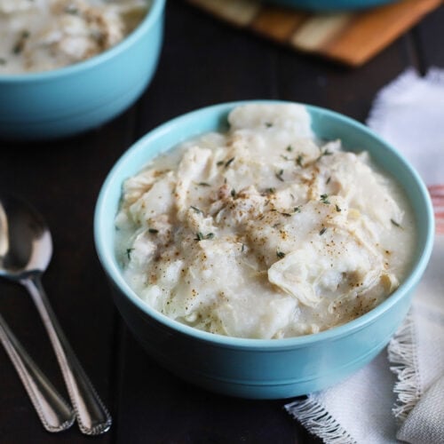homemade chicken and dumplings sprinkled with black pepper and thyme in a blue bowl