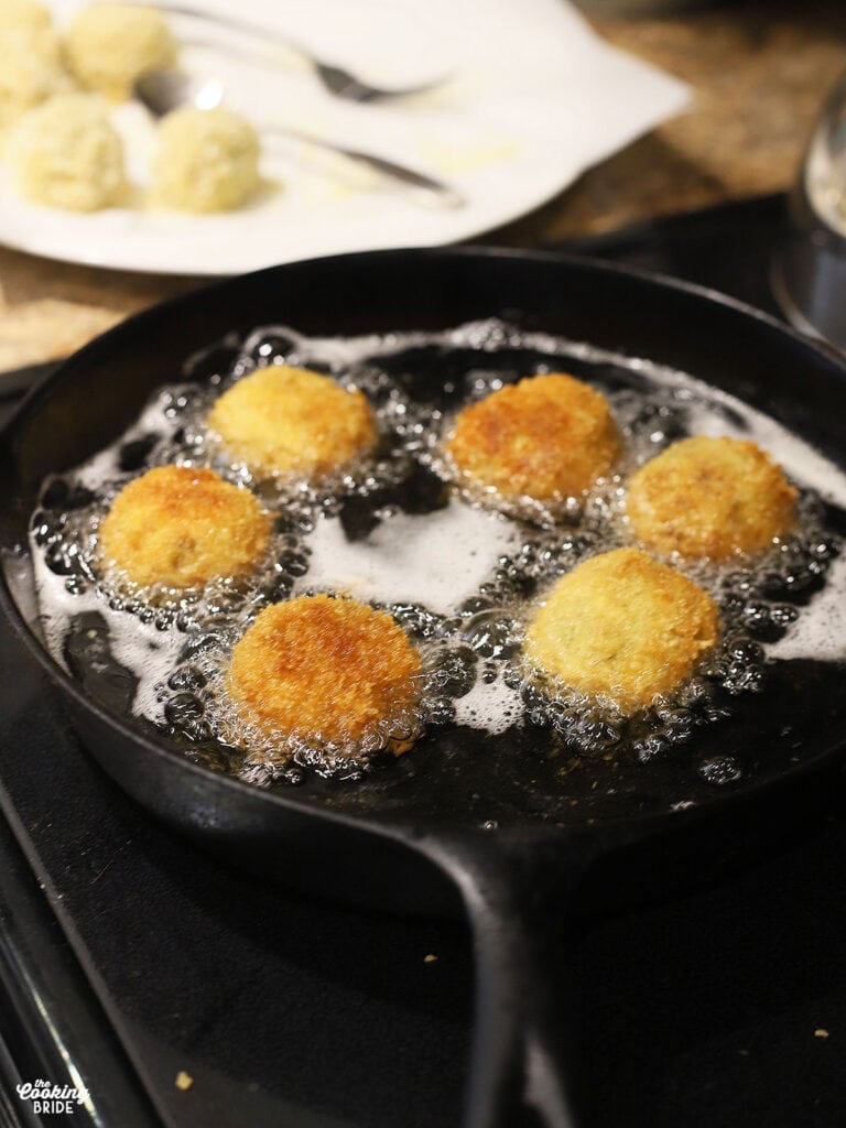 six boudin balls frying in a cast iron skillet