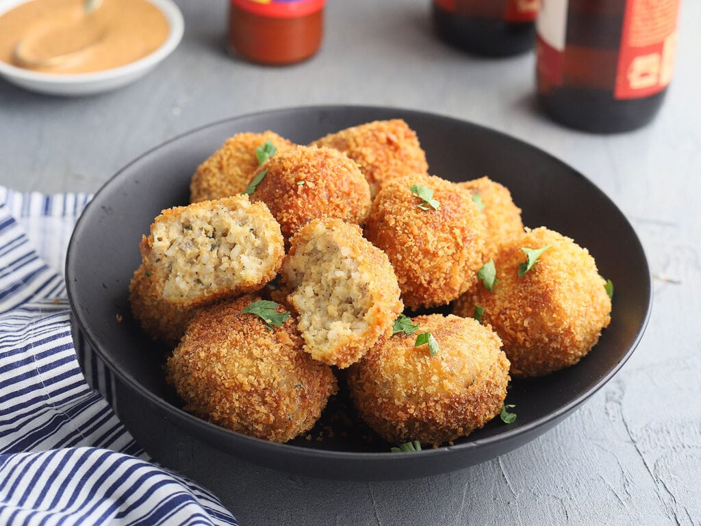 fried boudin balls in a black serving bowl with one broken open to show the inside