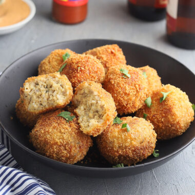 fried boudin balls in a black serving bowl with one broken open to show the inside