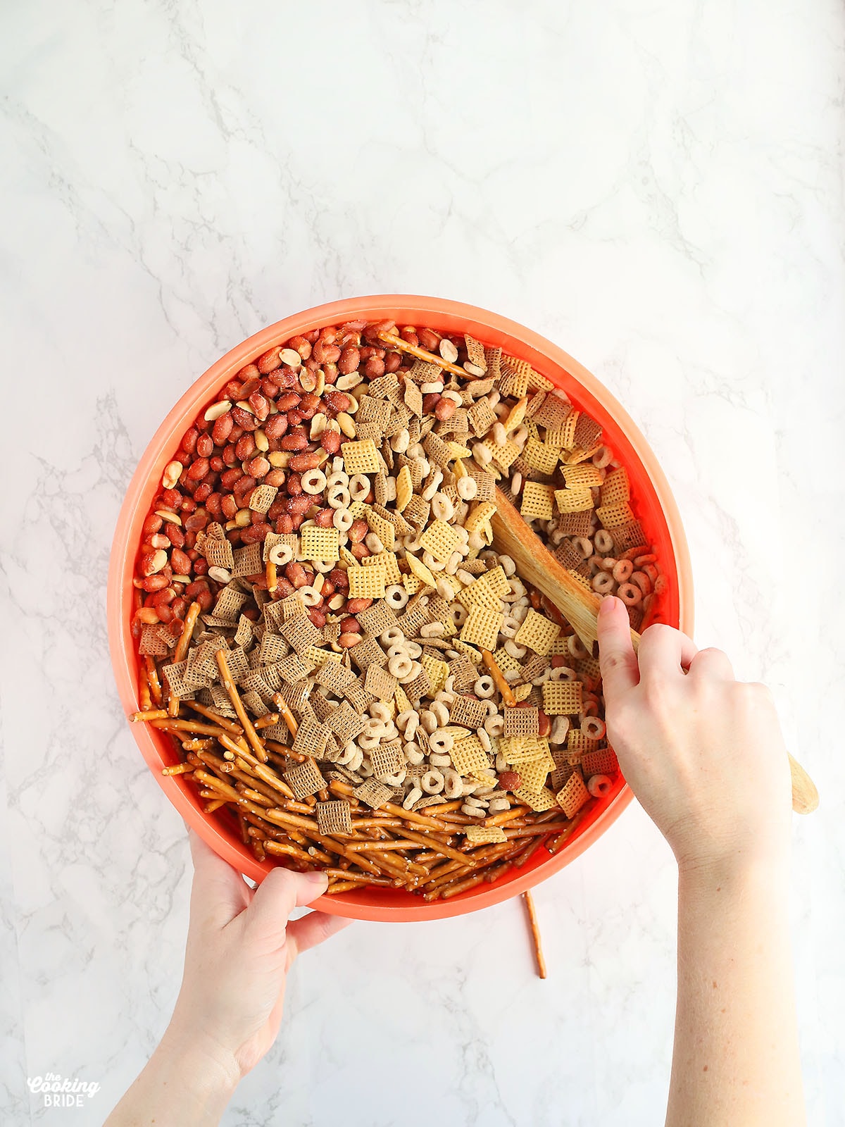 hand stirring chex mix ingredients in a large orange plastic bowl