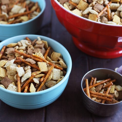 blue bowl full of chex mix with metal measuring cup to the side