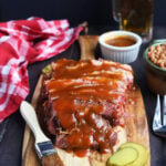 sliced brisket on a cutting board with potato salad, cole slaw and baked beans to the side