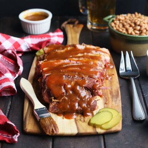 sliced brisket on a cutting board with potato salad, cole slaw and baked beans to the side