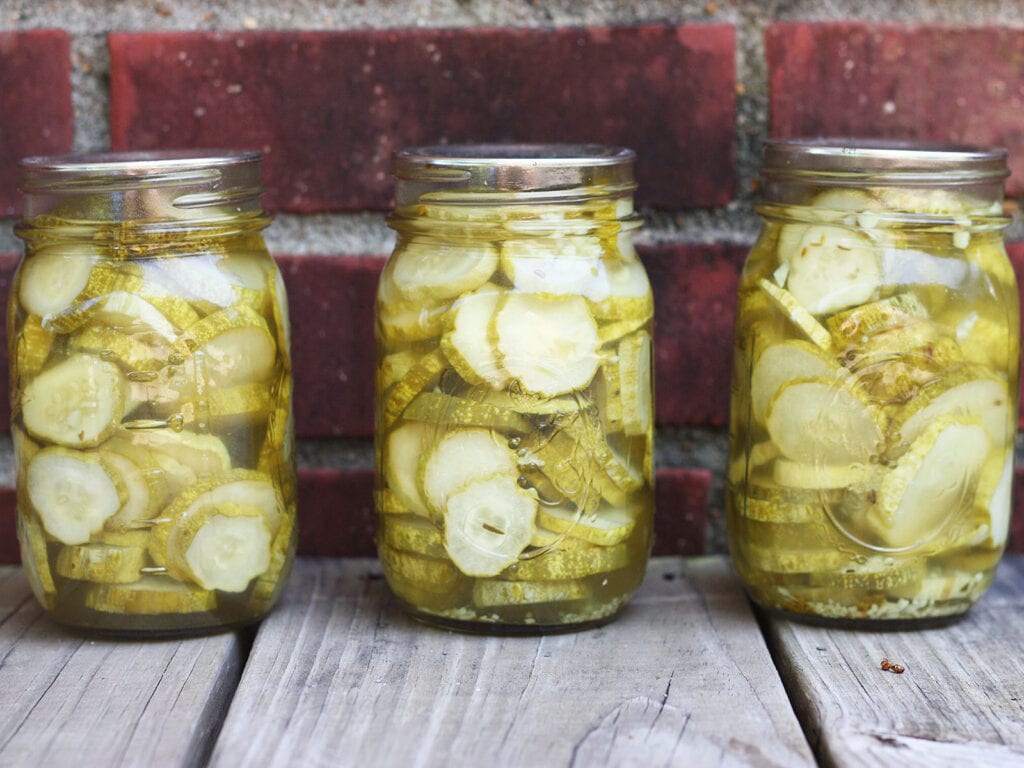 three sealed jars of sliced dill pickles on a worn wooden background with weathered brick in the background