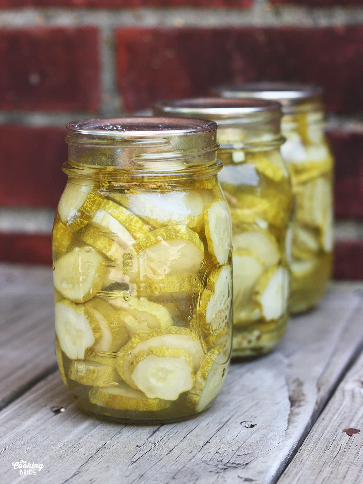 three sealed jars of sliced dill pickles on a worn wooden background with weathered brick in the background