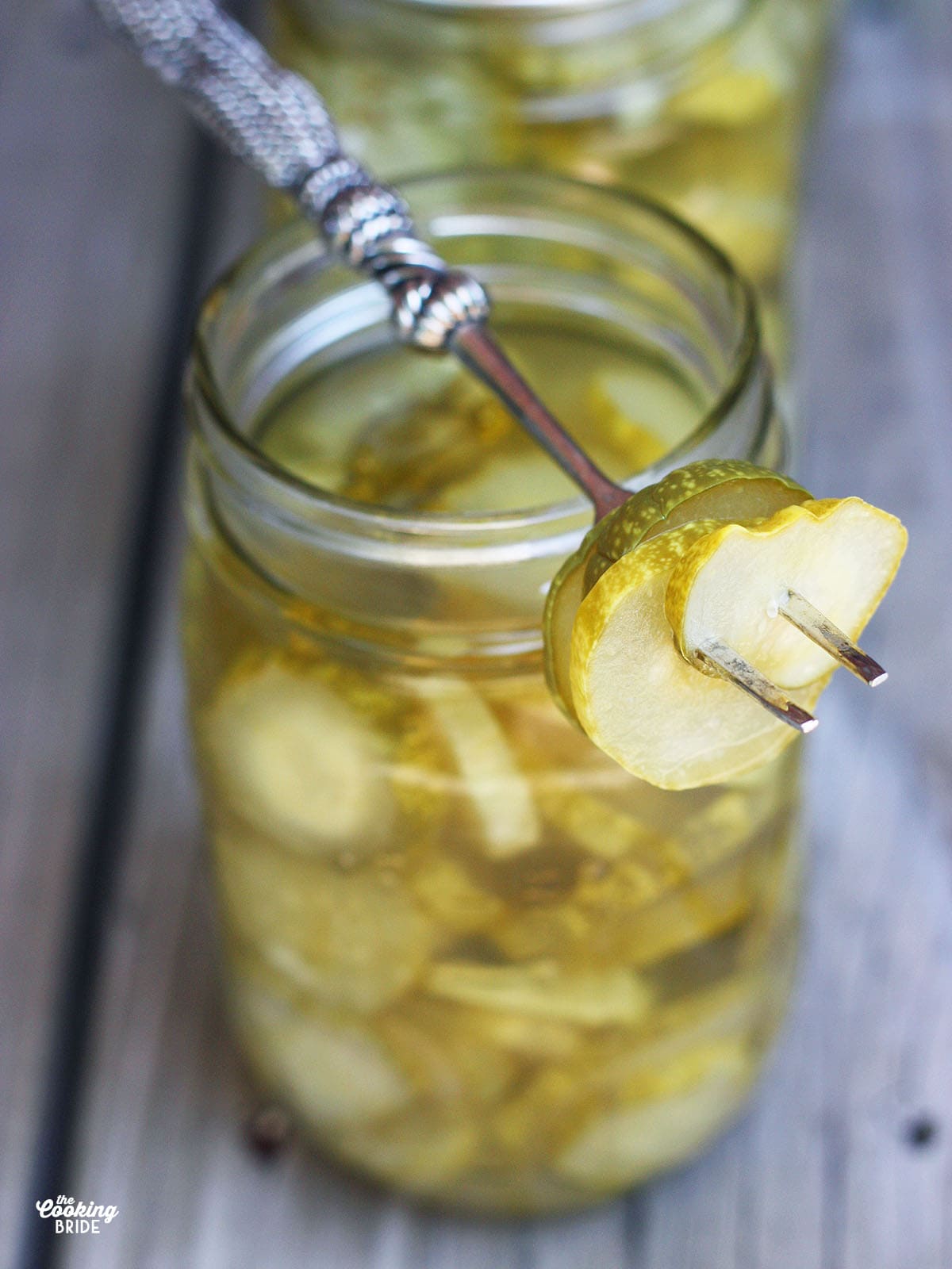 four dill pickle slices speared on a silver fork resting on top of a mason jar of pickles