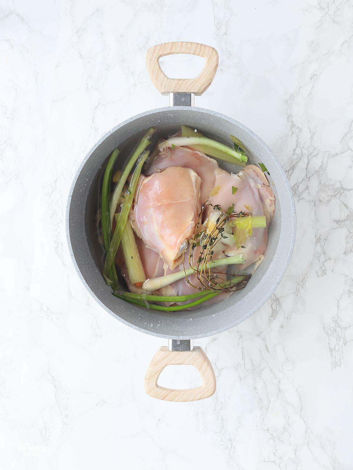 raw chicken pieces in a grey soup pot will with water and aromatic herbs and vegetables