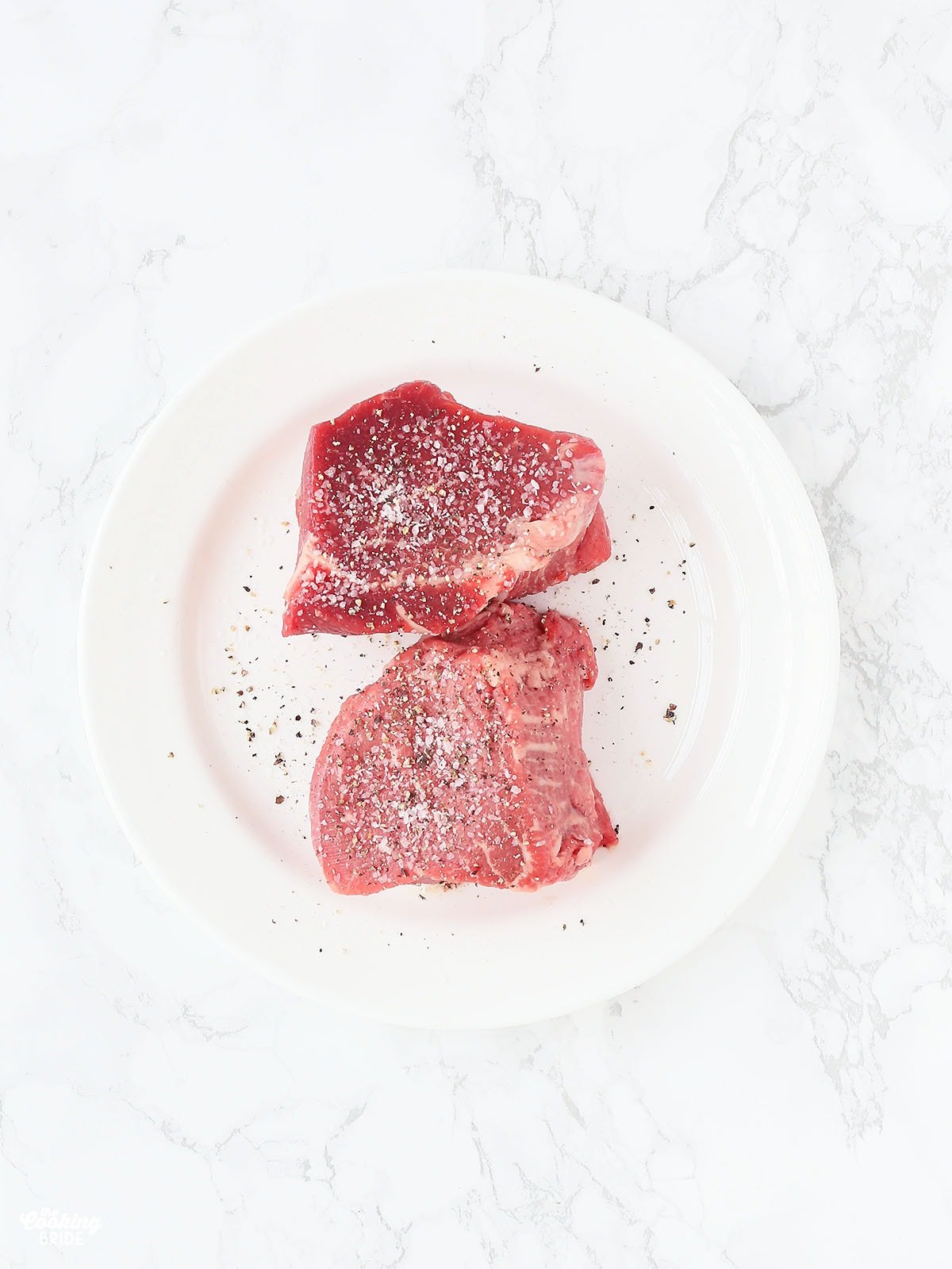 two raw filets seasoned with salt and pepper on a white plate