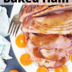 overhead shot of bourbon glazed baked ham on a white platter surrounded by orange slices
