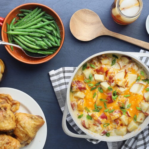cheesy ranch roasted potatoes in a white casserole dish with fried chicken and green beans on the side