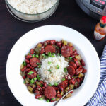 white dish of red beans and rice with a metal spoon, bowl of cooked rice and an Instant pot to the side