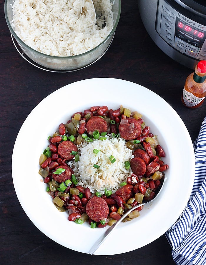 white dish of red beans and rice with a metal spoon, bowl of cooked rice and an Instant pot to the side
