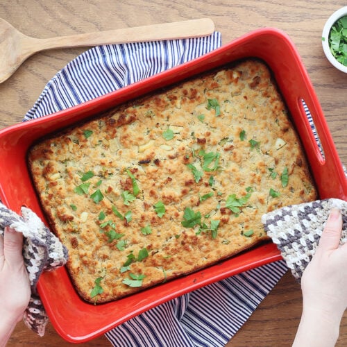 pair of hands placing a red pan of southern cornbread dressing with chicken on a table