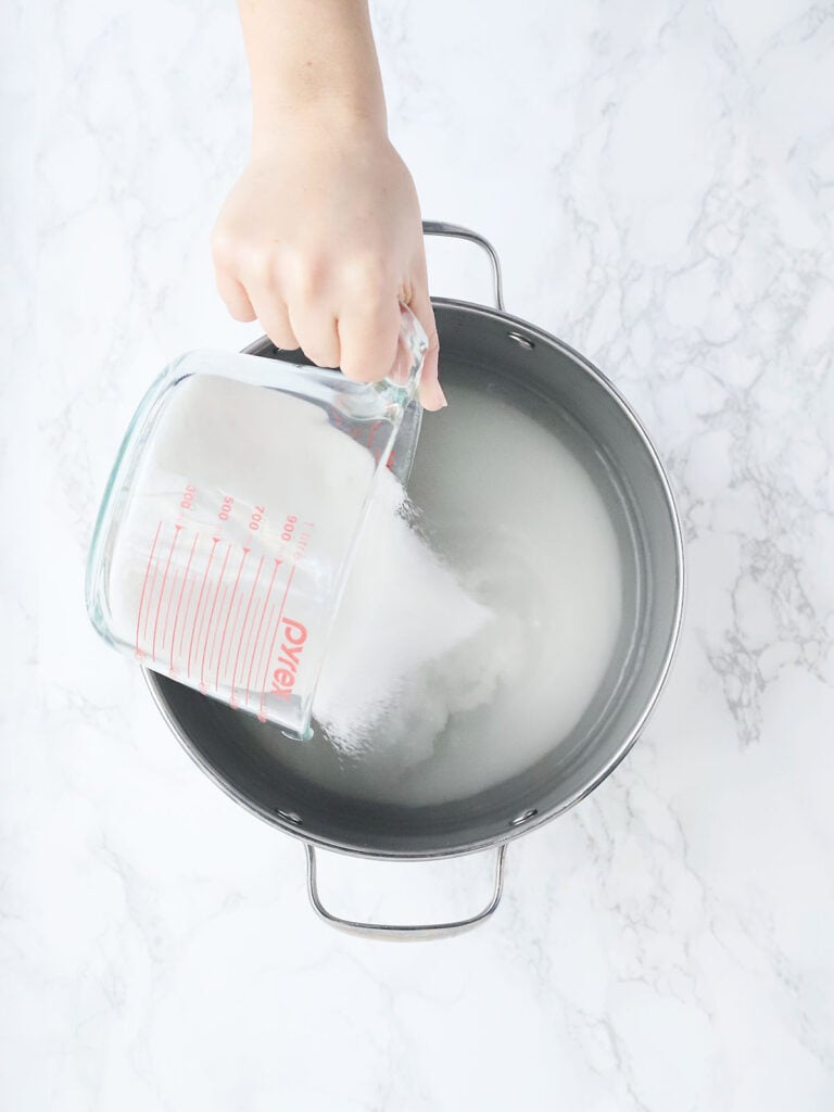 hand pouring sugar into a stock pot of water