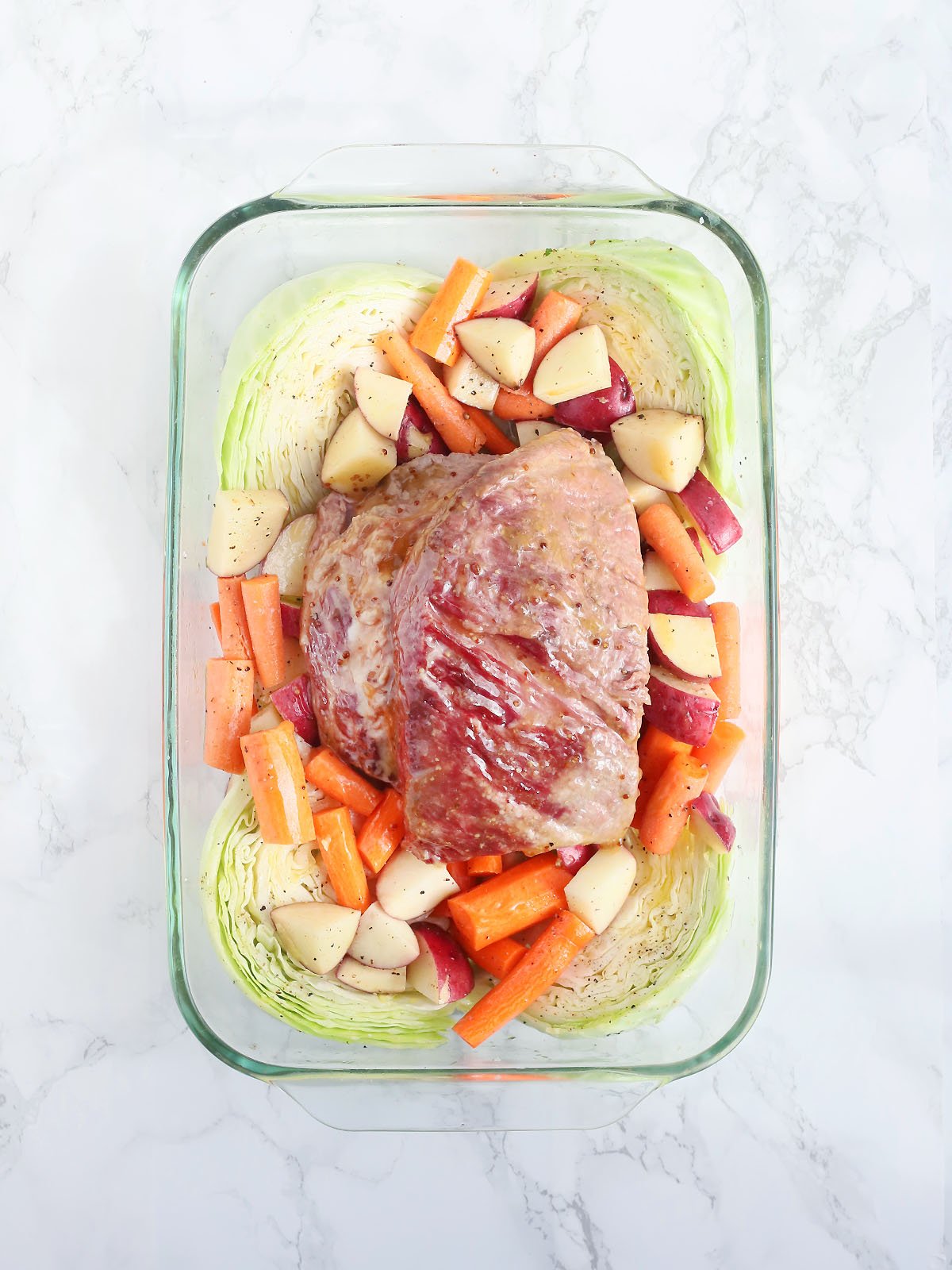 unbaked glazed corned beef brisket in a baking dish with cabbage, carrots and potatoes