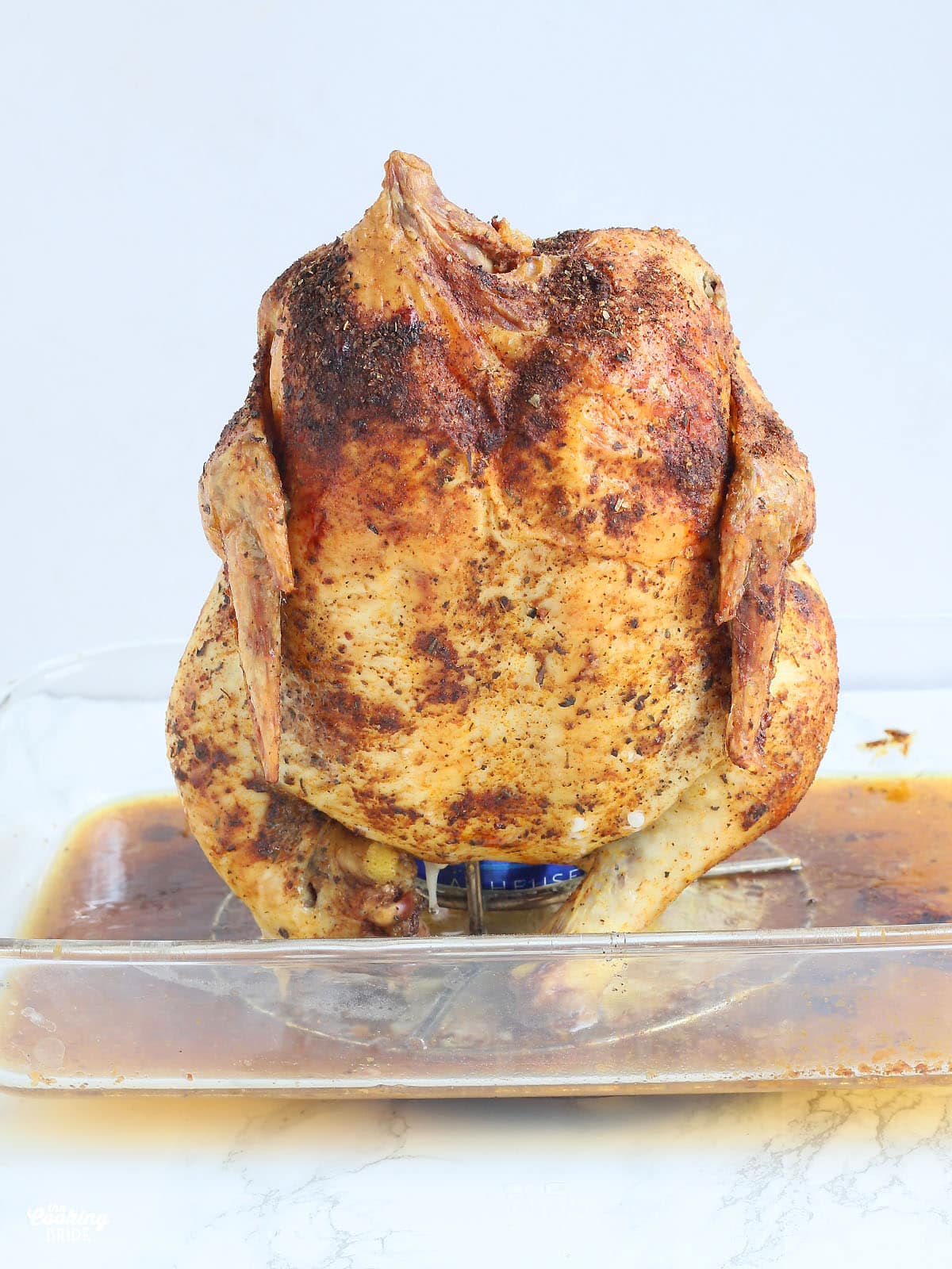 roasted beer can chicken sitting on a roaster in a glass casserole dish