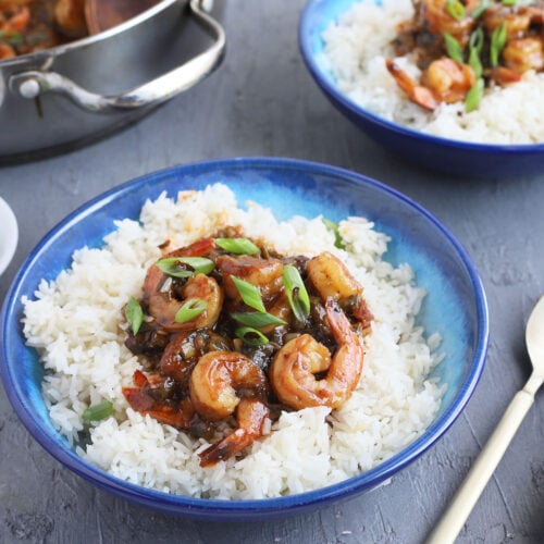 cooked Cajun shrimp laying on a bed of rice garnished with green onions in a blue bowl.