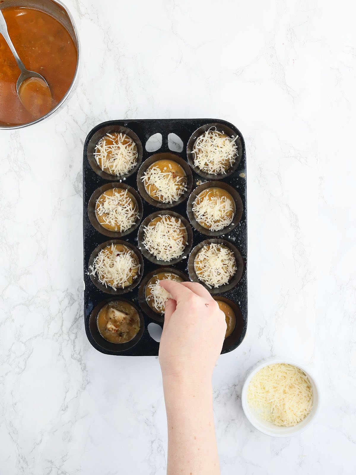 hand sprinkling parmesan cheese over the tops of oysters in a muffin pan