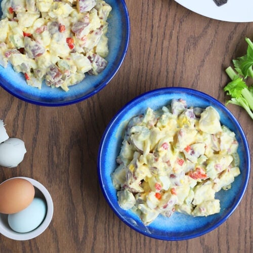 overhead shot of two blue bowls filled with potato salad, celery stalks, colorful hardboiled eggs and roast chicken to the side