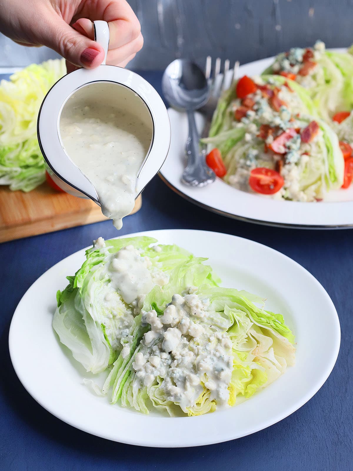 hand pouring blue cheese dressing over a lettuce wedge on a white plate